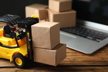 Toy forklift with boxes near laptop on wooden table. Logistics and wholesale conceptの写真素材