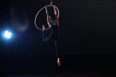 Young woman performing acrobatic element on aerial ring against dark backgroundの写真素材