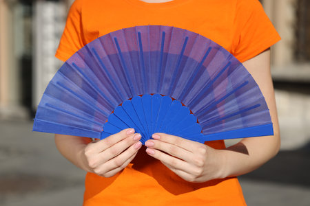 Woman with blue hand fan outdoors, closeupの写真素材