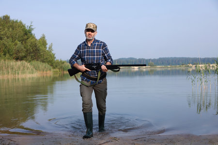 Man with hunting rifle near lake outdoorsの写真素材