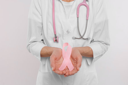 Doctor with stethoscope holding pink ribbon on white background, closeup. Breast cancer awarenessの写真素材
