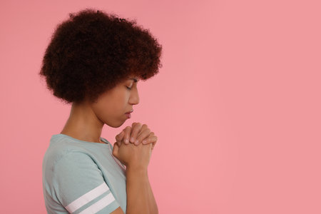 Woman with clasped hands praying to God on pink background. Space for textの写真素材