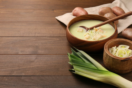 Bowl of tasty leek soup, spoon and ingredients on wooden table. Space for textの写真素材