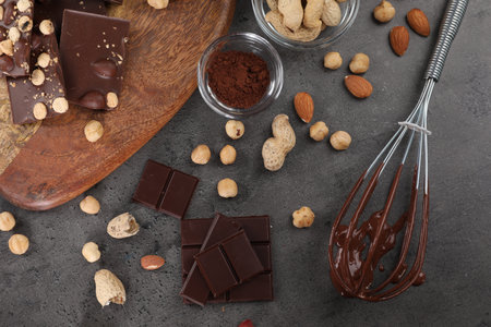 Whisk with chocolate cream and ingredients on gray table, flat lay