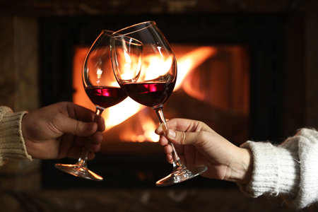 Couple clinking glasses of wine near fireplace at home, closeupの写真素材