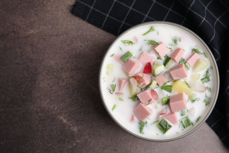 Delicious cold summer soup (okroshka) with boiled sausage in bowl on brown table, top view. Space for textの写真素材