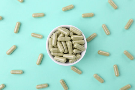 Bowl with vitamin capsules on turquoise background, flat layの写真素材