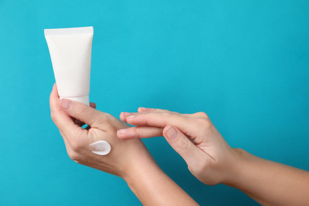 Woman with tube applying cosmetic cream onto her hand on light blue background, closeup. Space for textの写真素材