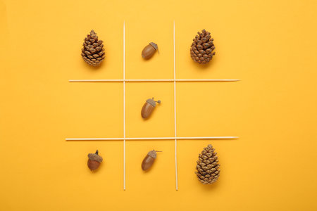 Tic tac toe game made with acorns and pine cones on yellow background, top viewの写真素材