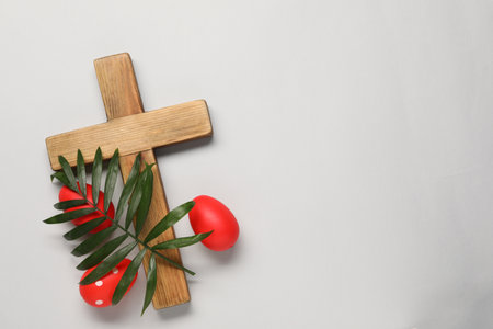 Wooden cross, painted Easter eggs and palm leaf on light gray background, flat lay. Space for textの写真素材