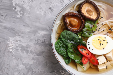 Delicious vegetarian ramen with egg, mushrooms, tofu and vegetables in bowl on gray table, top view and space for text. Noodle soupの写真素材