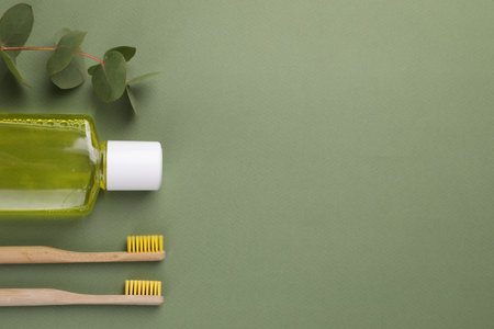 Fresh mouthwash in bottle, toothbrushes and eucalyptus branch on green background, flat lay. Space for textの写真素材