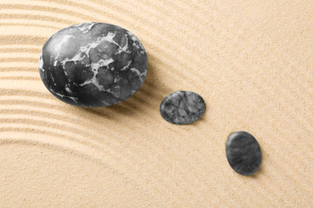Zen garden stones on beige sand with pattern, flat lay