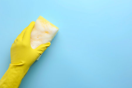 Cleaner in rubber glove holding sponge with foam on light blue background, top view. Space for textの写真素材