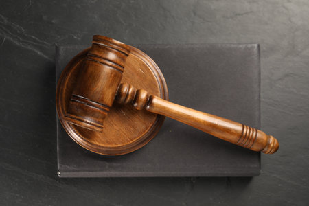 Wooden gavel, sound block and book on dark textured table, top view