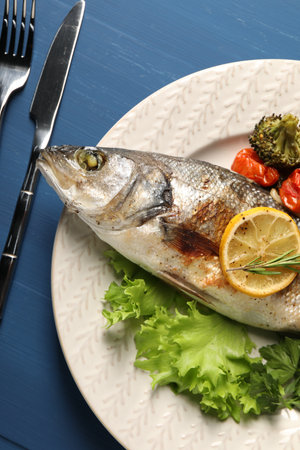 Delicious baked fish and vegetables served on blue wooden table, top viewの写真素材