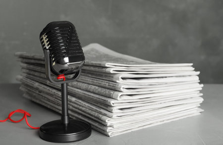 Newspapers and vintage microphone on light gray stone table. Journalist's work