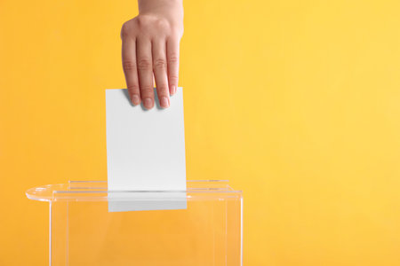 Woman putting her vote into ballot box on orange background, closeup. Space for textの写真素材