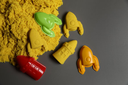 Different figures made of yellow kinetic sand and plastic toys on gray background, flat lay. Space for textの写真素材