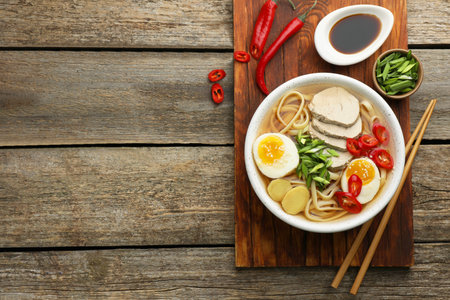 Delicious ramen in bowl served on wooden table, flat lay and space for text. Noodle soup
