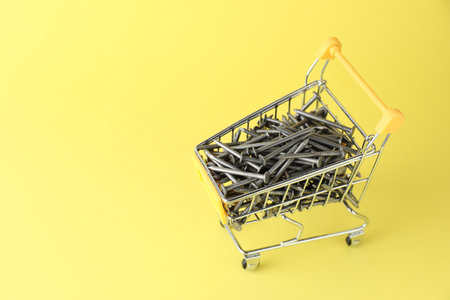 Metal nails in shopping cart on yellow background, space for textの写真素材