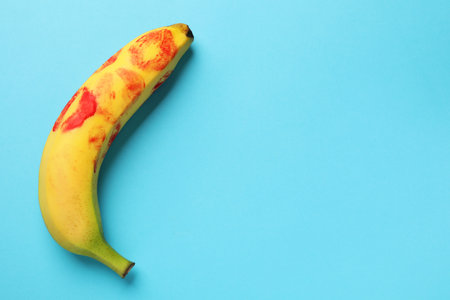 Banana with red lipstick marks on light blue background, top view with space for text. Sex conceptの写真素材