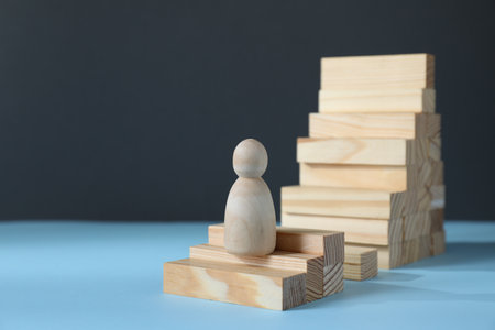 Stairs of blocks with gap as barrier and wooden human figure on light blue surface, space. for text. Path to growth and successの写真素材