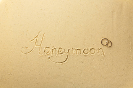 Word Honeymoon written on sand and two golden rings, top viewの写真素材