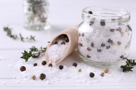 Salt with peppercorns in glass jar, thyme and scoop on white wooden table, closeupの写真素材