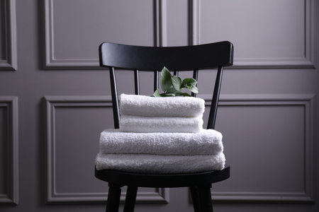 Stacked soft towels and green leaves on black chair indoorsの写真素材