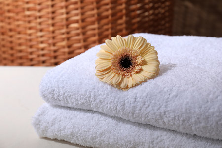 Stacked terry towels and flower on white table, closeup. Space for textの写真素材