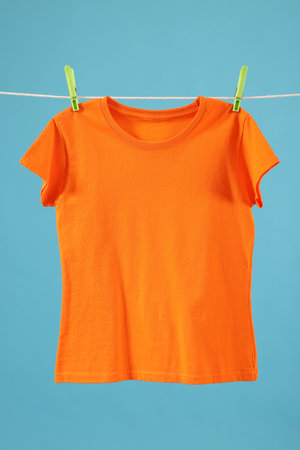 One orange t-shirt drying on washing line against light blue backgroundの写真素材