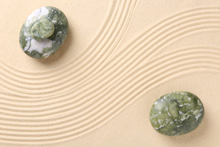 Zen concept. Stones and pattern on beige sand, flat lay. Space for text