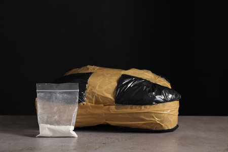 Smuggling, drug trafficking. Package with narcotics and utility knife on gray table against black...