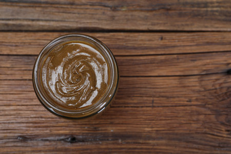 Tasty nut paste in jar on wooden table, top view. Space for text