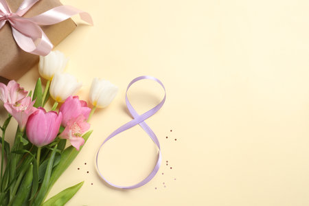 8th of March greeting card design with violet ribbon, gift box, beautiful flowers and space for text on beige background, flat lay. International Women's dayの写真素材
