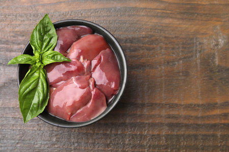 Bowl of raw chicken liver with basil on wooden table, top view. Space for textの写真素材
