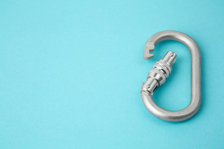 One metal carabiner on light blue background, closeup. Space for text