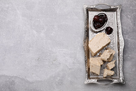 Pieces of tasty halva and dates served in vintage tea set on light gray table, top view. Space for...