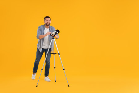 Happy astronomer with telescope on orange background. Space for textの写真素材