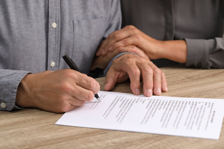 Couple signing document at wooden table, closeupの写真素材