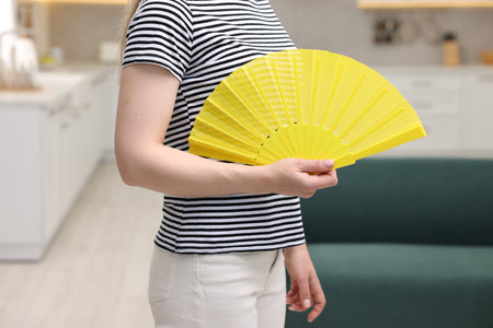 Woman with yellow hand fan at home, closeupの写真素材