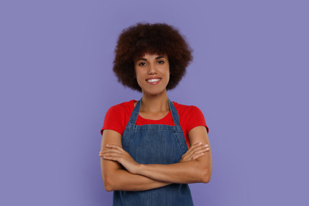 Portrait of happy young woman in apron on purple backgroundの写真素材