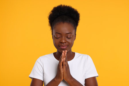 Woman with clasped hands praying to God on orange backgroundの写真素材