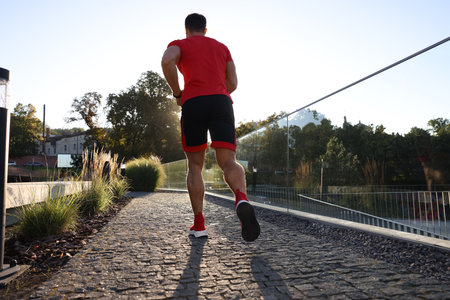 Man running outdoors on sunny day, back view