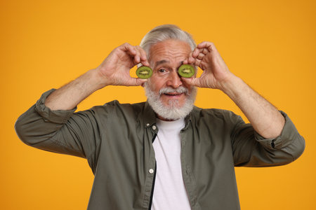 Senior man holding halves of kiwi on orange backgroundの写真素材