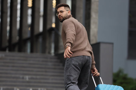Being late. Worried man with suitcase running towards building outdoors, space for text