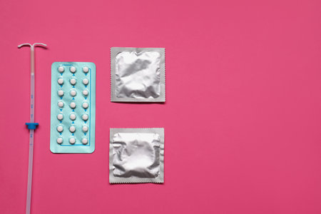 Contraception choice. Pills, condoms and intrauterine device on magenta background, flat lay. Space for textの写真素材