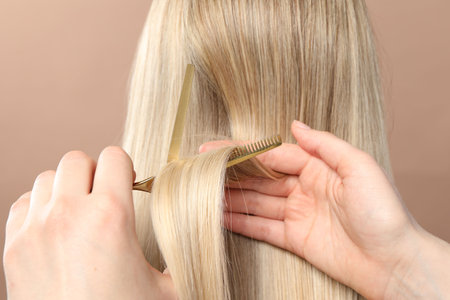 Hairdresser cutting client's hair with scissors on beige background, closeupの写真素材