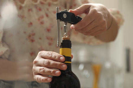 Woman opening wine bottle with corkscrew on blurred background, closeupの写真素材